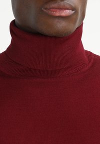 Bordeauxrode coltrui met een geribbelde textuur en een aansluitend ontwerp, gemaakt van een zachte gebreide stof.