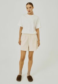 White cotton t-shirt with short sleeves and a round neck, paired with beige linen shorts featuring an elastic waistband and minimal texture.