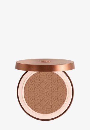 Kompakt puddermakeup med præget geometrisk mønster, indeholdt i en rund, metallisk bronzefarvet etui med delvist åben låg.