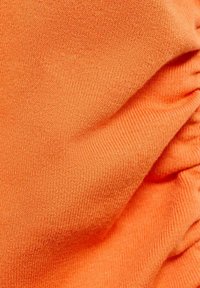 Oranžová látka s textúrovaným pletením, s jemnými nariaseniami vytvárajúcimi mäkké záhyby. Materiál vyzerá ľahký a pružný.