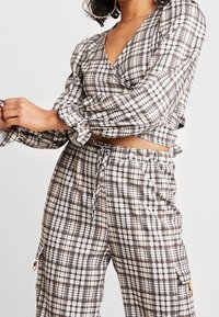 Crop-Top- und Hosen-Set im karierten Muster. Das Top hat lange Puffärmel und einen tiefen V-Ausschnitt; die Hose hat einen elastischen Bund und Taschen.