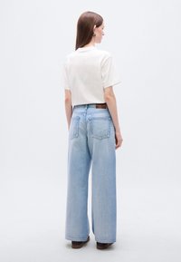 Φαρδιά τζιν παντελόνια σε ανοιχτό μπλε με ψηλή μέση, συνδυασμένα με cropped λευκό t-shirt. Διαθέτουν δύο πίσω τσέπες και καφέ ετικέτα. Φορούνται με επίπεδα παπούτσια.