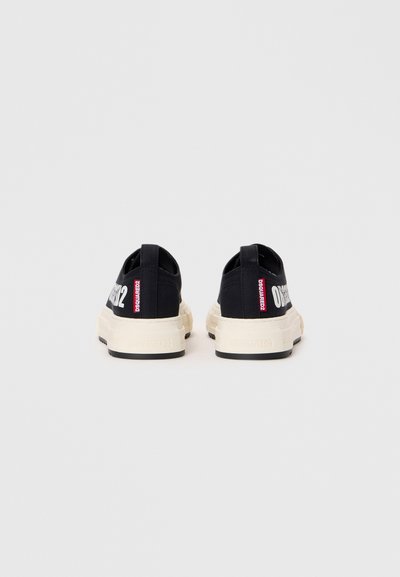 Baskets noires en toile avec un design bas, semelles en caoutchouc de couleur crème et logo blanc sur le talon. Présente des accents rouges contrastants.