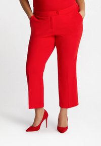 Czerwone, krótkie spodnie wykonane z gładkiego materiału, z przednimi kieszeniami i zapięciem na guzik, zestawione z czerwonymi szpilkami.