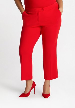 Pantaloni cropped rossi realizzati in tessuto morbido, con tasche frontali e chiusura a bottone, abbinati a tacchi alti rossi.