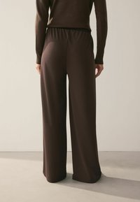 Braune, weite Hose aus einem weichen, glatten Stoff mit einem elastischen Bund, minimalistischem Design und sauberem Finish.
