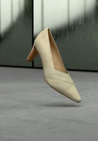 Chaussure à talon haut en daim beige avec un bout pointu, un détail texturé sur la tige et un talon bloc en bois. Design simple, sans accents supplémentaires.