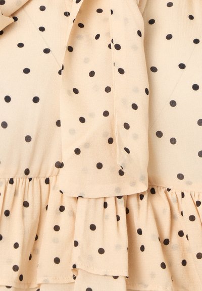 Μπεζ ύφασμα με μαύρα πουά, με ραμμένα επίπεδα και μανίκι με φαρδιά, ρέουσα μανσέτα.