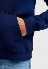 Námořnická modrá mikina s boční kapsou, žebrovanými zápěstími a měkkou texturou. Viditelné švy na lemu a kapse. Ležérní design.