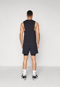 Μαύρο αμάνικο τοπ και σκούρα σορτς, με άνετη εφαρμογή. Φοριέται με άσπρες κάλτσες και μαύρα αθλητικά παπούτσια. Απλός σχεδιασμός.