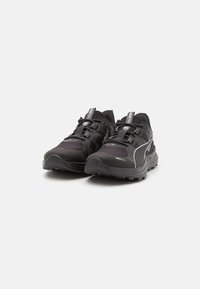 Black trail running shoes with a textured upper, reflective accents, and a rugged sole. Features a secured lace system for fit adjustment.