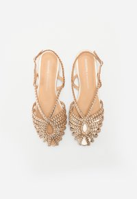 Gouden sandalen met bandjes en een geweven ontwerp, met een opvallend decoratief detail aan de voorkant en een open teen. Platte zool.
