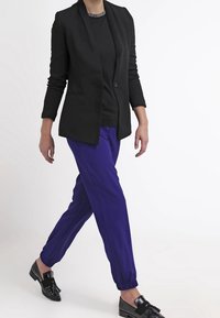 Zwart getailleerd colbert met lange mouwen, gecombineerd met paarse broek met elastische boorden en zwarte loafers. Eenvoudig ontwerp, zonder patronen of accenten.