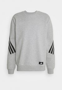 Sweatshirt Adidas gris clair avec des rayures diagonales noires sur les manches et un petit patch avec le logo Adidas près de l'ourlet, col rond et poignets côtelés.