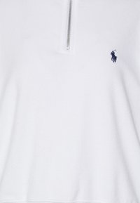 Maglione bianco con zip a un quarto sul davanti, realizzato in tessuto morbido. Presenta un piccolo logo scuro nella zona sinistra del petto. Texture liscia.