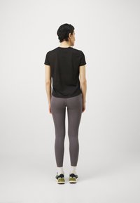 Svart t-skjorte med korte ermer og avslappet passform, sammen med grå leggings. Antrekket har en glatt tekstur og atletisk stil på skoene med hvite sokker.