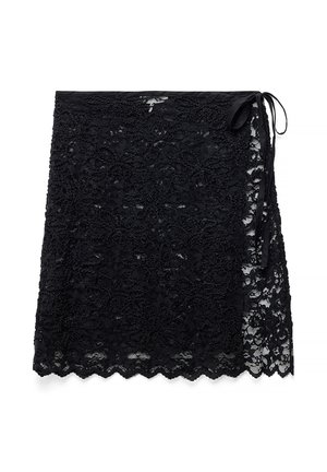 Falda envolvente de encaje negro con patrón floral y dobladillo con borde festoneado, con cierre de lazo lateral.