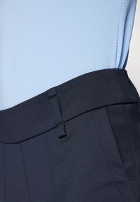 Marineblaue maßgeschneiderte Hosen mit glatter Textur und breitem Bund; kombiniert mit einem hellblauen strukturierten Hemd mit Wabenmuster.