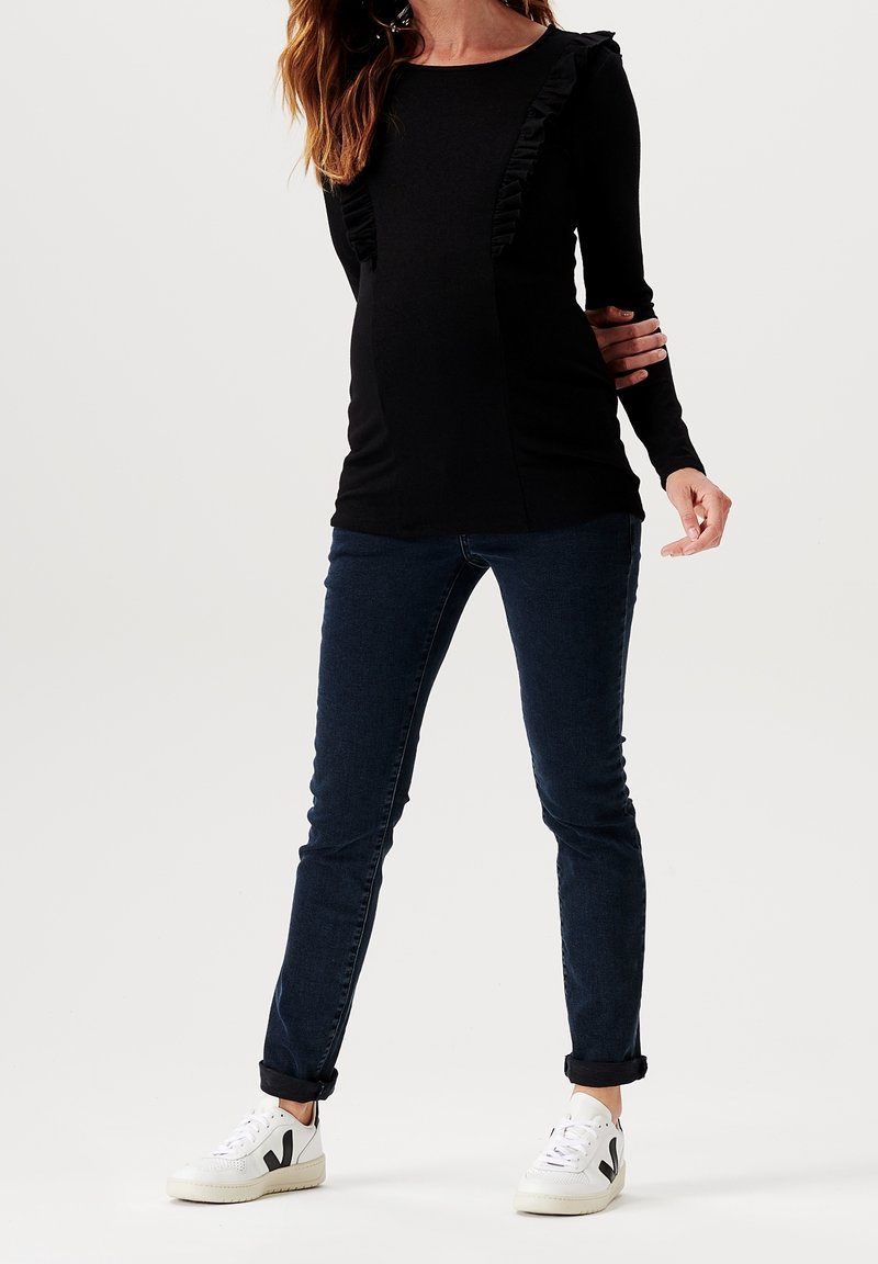 Haut noir à manches longues avec des accents froncés, associé à un jean skinny bleu foncé et des baskets blanches avec des détails noirs.