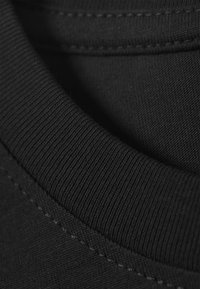 Black cotton t-shirt fabric with a ribbed neckline, featuring fine stitching and a soft texture. Close-up view of material details.