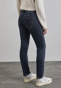 Mörkblå jeans med en figurnära passform, med bakfickor och medelhög midja, i kombination med vita och beige sneakers.
