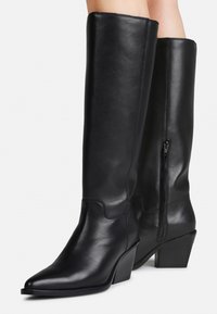 Bottes en cuir noir montantes, avec un bout pointu, une surface texturée, une couture discrète et une fermeture éclair sur le côté ; design à talon empilé.