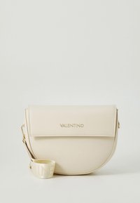 Cream leather crossbody bag with a rounded shape, magnetic flap closure, gold logo, and a detachable strap featuring the brand name.