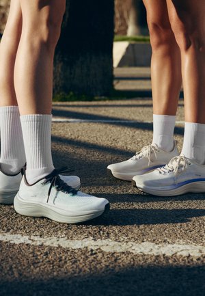 Dva lidé ve bílých sportovních botách a ponožkách stojí naproti sobě na venkovním dlážděném povrchu s namalovanou linií.