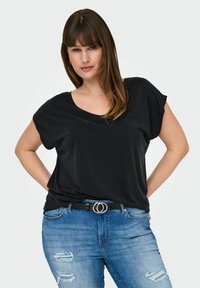 Haut noir à manches courtes avec un décolleté large, associé à un jean bleu déchiré et une ceinture noire avec une boucle double en argent.