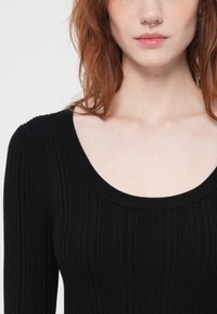 Black ribbed sweater featuring a wide scoop neckline, long sleeves, and a close fit, showcasing a textured, knit fabric.