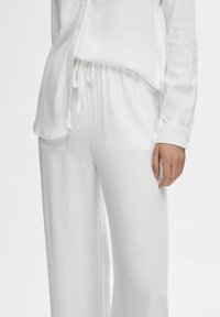 Witte, lichtgewicht blouse met knoopsluiting aan de voorkant, lange mouwen en een zachte textuur. Gecombineerd met witte, loszittende broek met een tasband.