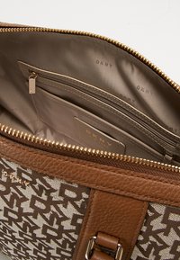 Brązowa skórzana torba z teksturowanym wnętrzem, z beżowym wnętrzem i kieszenią na zamek. Widoczne złote akcenty i logo marki.