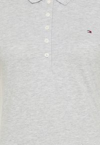 Grijze poloshirt van zachte stof, met een kraag, een placket met zes knopen en een klein logoaccent in rood, wit en blauw.