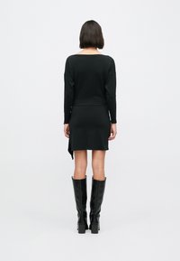 Czarna bluzka z długim rękawem i szerokim dekoltem, zestawiona z czarną sukienką do kolan z asymetrycznym dołem. Gładka tekstura.