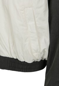 Chaqueta ligera con sección superior blanca y sección inferior negra, que presenta un dobladillo fruncido y un bolsillo lateral con apertura plana.