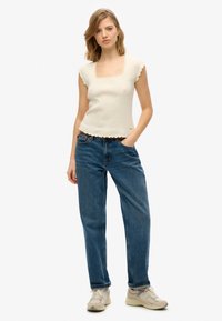 Crème gekreukt crop top met geschulpte randen, vierkante halslijn en korte mouwen; gecombineerd met losse blauwe jeans en lichte sneakers.