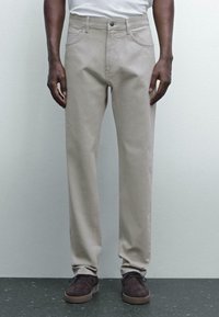 Pantaloni in cotone beige con vestibilità dritta, dotati di tasche frontali, chiusura con bottone e sottili dettagli di cucitura.