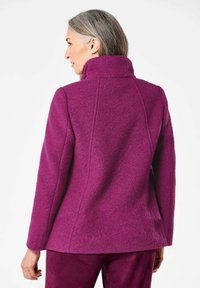 Fleecejacke in lebhaftem Lila mit hohem Kragen, strukturiertem Finish und vertikalen Nähten. Bietet eine taillierte Passform und einen mittellangen Schnitt.