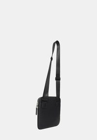 Borsa a tracolla nera con un motivo texture, chiusura con zip e tracolla regolabile. Realizzata in materiale morbido, forma quadrata, design minimalista.