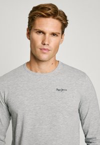 Grijs langemouwenshirt van een gladde stof, met een ronde hals en een klein geborduurd logo op de linkerborst.
