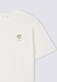 T-shirt in cotone color crema con scollatura rotonda. Presenta un piccolo design a conchiglia ricamato e la parola "Sunshine" sottostante.