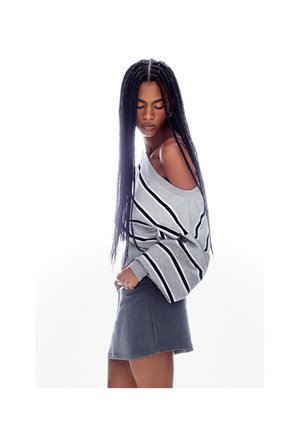 Maglione grigio a righe con design a spalle scoperte, caratterizzato da maniche ampie. Abbinato a una gonna di jeans grigia corta.