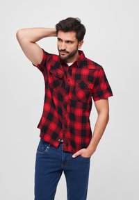 Camisa de cuadros en rojo y negro de manga corta con dos bolsillos en el pecho, cierre de botones y un corte relajado. Fabricada con tejido tejido y con una textura suave.