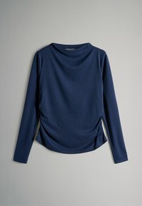 Granatowa bluzka z długim rękawem, wykonana z miękkiego materiału, z dekoltem w serek, marszczeniami po bokach oraz luźnym krojem.