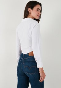 Witte longsleeve met kraag, gecombineerd met donkerblauwe denim jeans met een leren patch en dubbel gestikte achterzakken.