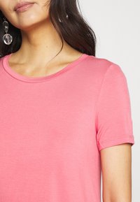 Růžové tričko s krátkým rukávem a kulatým výstřihem, vyrobené z měkké a hladké tkaniny. Švy podél rukávů a těla.