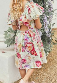 Vestido de estampado floral en tela ligera que presenta rosas en tonos rosa, púrpura y amarillo, con mangas cortas acampanadas y un corte en la espalda, además de una cintura elástica.