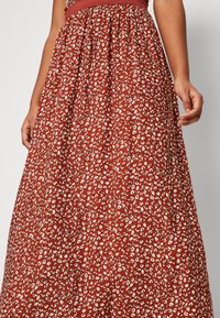 Rotes Maxikleid mit weißem Blumenmuster, geraffter Taille und weichem Material. Verfügt über einen breiten elastischen Bund in der Taille für hohen Tragekomfort.