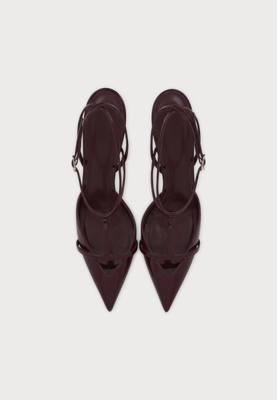 Ζευγάρι σκούρα μπορντό μυτερά πέδιλα slingback με λεπτές ζώνες στον αστράγαλο και πλαϊνές αγκράφες σε ανοιχτό φόντο.