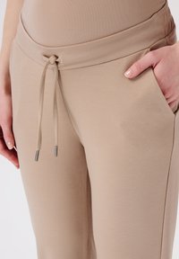 Beige joggers met een trekkoord in de taille, textuurstof, metalen aglets aan de touwtjes en zijzakken voor praktisch gebruik.